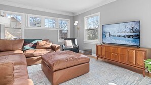 Una sala de estar con un sofá grande tipo seccional, un mueble de madera, un televisor y una ventana con vista a árboles.