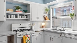 Una cocina moderna con armarios blancos, una estufa a gas, horno integrado y un amplio ventanal que proporciona luz natural.
