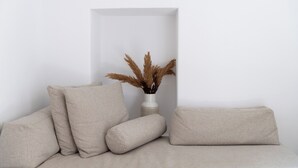 Un soggiorno dal design minimalista con un divano e cuscini, un vaso con piante essiccate e una parete bianca.