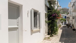 Una stretta strada acciottolata fiancheggiata da edifici bianchi con persiane e un piccolo albero con fiori rosa.