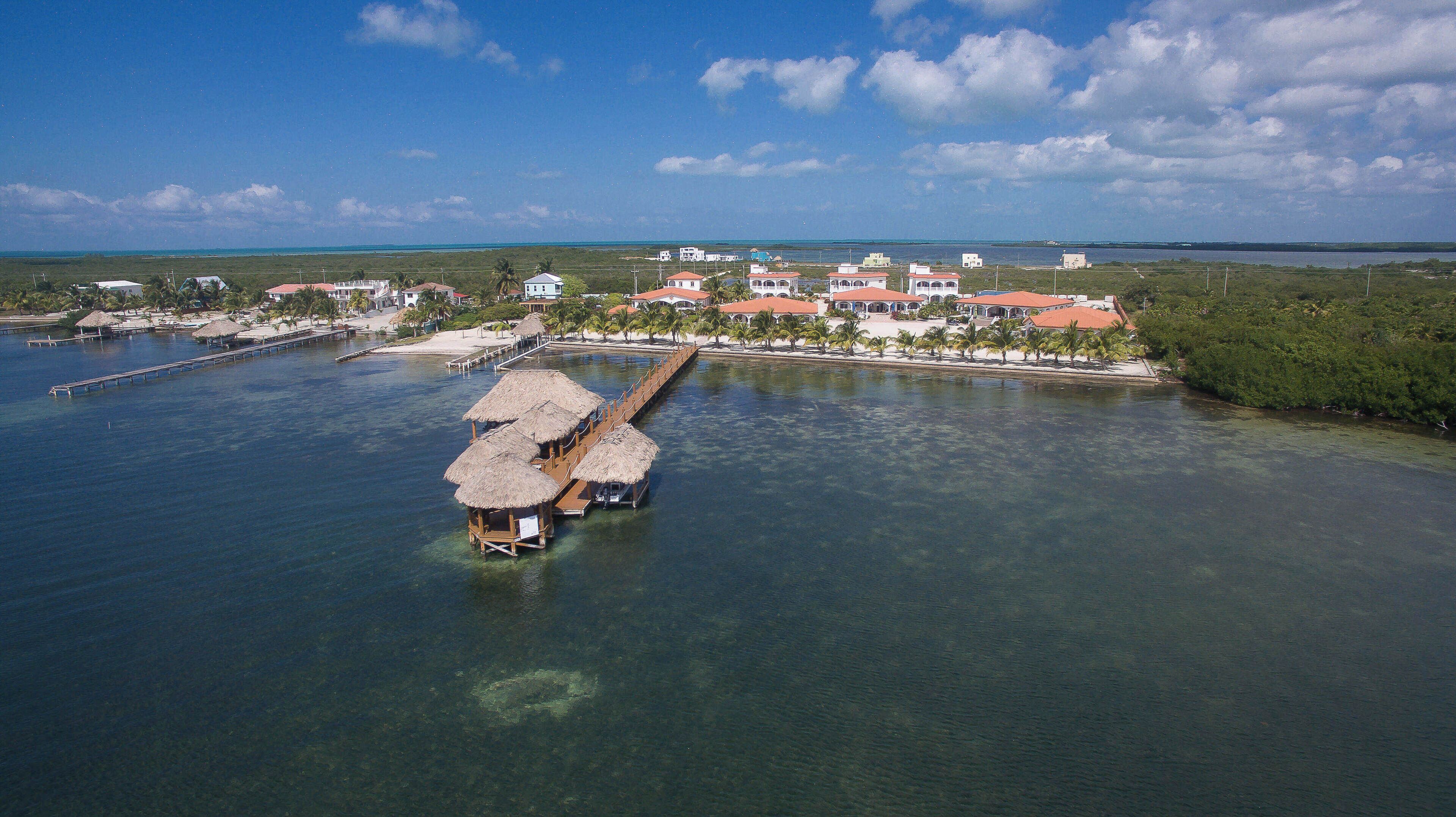 Luftaufnahme eines Küstenresorts mit Überwasservillen, einer Pier und einem Strandbereich.