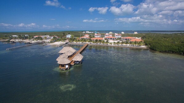 An aerial view of a coastal resort with overwater bungalows, a pier, and a beach area.