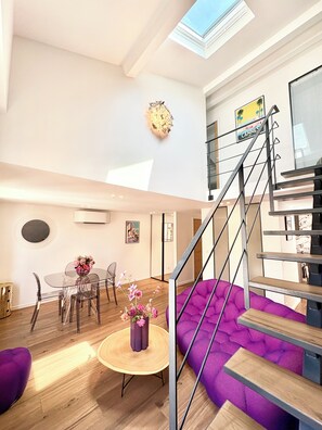 A modern interior with a dining area, a purple sofa, a staircase, and a skylight.