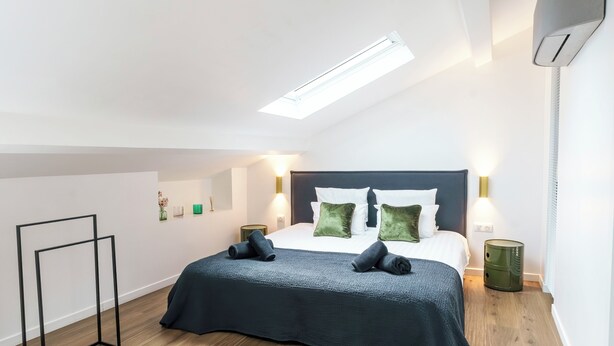 A modern bedroom with a skylight, a bed with green pillows, and a bedside table with a lamp.