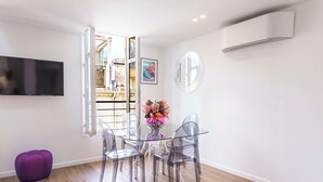 A modern living room with a glass dining table, clear chairs, a purple ottoman, and a mounted TV.