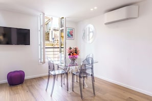 A modern living room with a glass dining table, clear chairs, a purple ottoman, and a mounted TV.