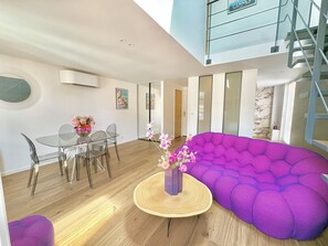A modern living space with a dining area, a purple sofa, and a staircase.