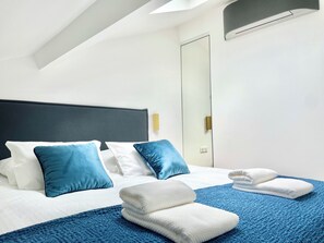 A hotel room with a bed, pillows, a blue blanket, and towels.