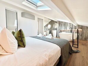 A modern hotel room with a skylight, a large bed, a bathroom with a bathtub, and a mirror.