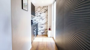 A hallway with a marble wall, a wooden floor, and a textured wall on the right.