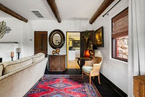 A cozy living room with a patterned rug, a sofa, a wooden cabinet, a wicker chair, and a large mirror on the wall. - Rock House Haven Retreat (Prescott)