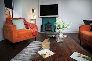 Una sala de estar con dos sofás naranja, una mesa de centro de madera, una chimenea y un televisor de pantalla plana montado encima.