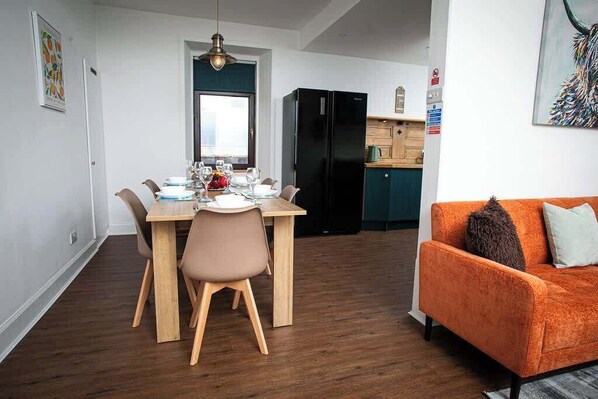 Un comedor con una mesa y sillas, un refrigerador negro y un sofá naranja.