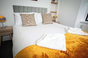 Ein Hotelzimmer mit Bett, Kissen, Nachttisch und Lampe sowie einem Fenster.