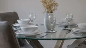 A dining table with white plates, bowls, and wine glasses, a vase with dried flowers, and a glass partition. - The Larky - Modern 2 Bed Cottage in Larkhall (Larkhall)