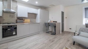 A modern kitchen with white cabinets, a gas stove, a microwave, and a built-in oven. There is a small bar area with stools and a window with a view of the outside. - The Larky - Modern 2 Bed Cottage in Larkhall (Larkhall)