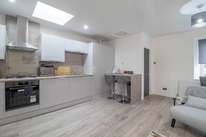 Une cuisine moderne avec des meubles blancs, une cuisiniĂšre Ă gaz, un four Ă micro-ondes et un four encastrĂ©. On y trouve Ă©galement un petit coin bar avec des tabourets et une fenĂȘtre donnant sur lâextĂ©rieur.