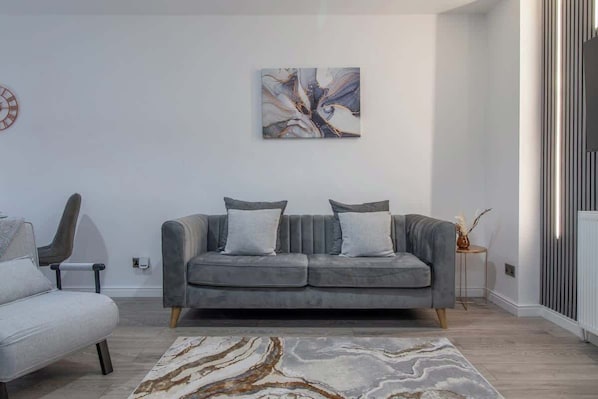 A modern living room with a grey sofa, a patterned rug, and a wall-mounted abstract painting.