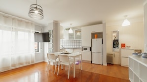 Une cuisine moderne avec des meubles blancs, une table à manger avec des chaises et des luminaires suspendus.
