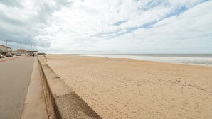 Une plage avec une promenade dallée et une petite barrière en béton.