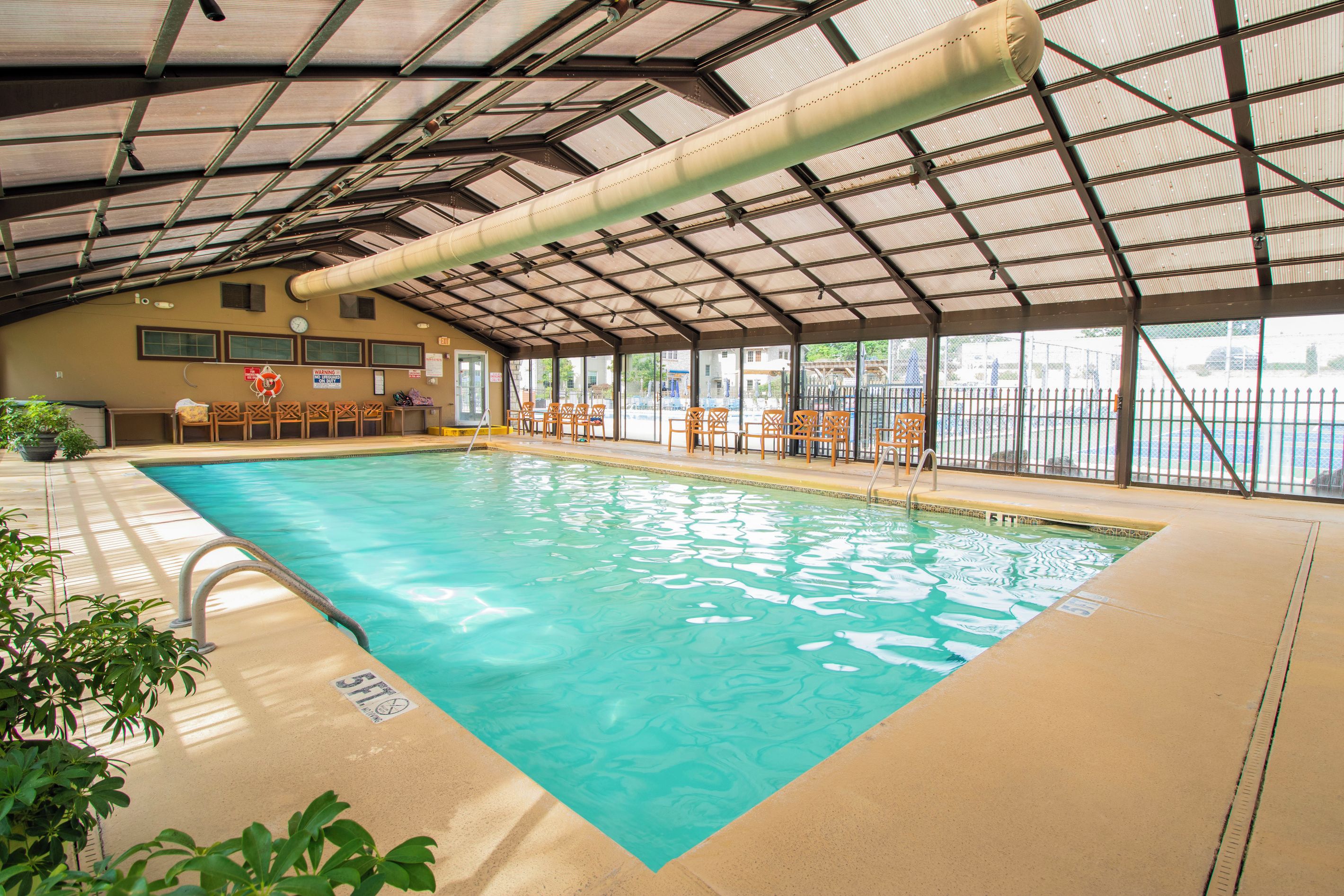 Une piscine intérieure à l’eau claire, entourée de chaises et dotée d’un espace abrité avec un toit en métal.