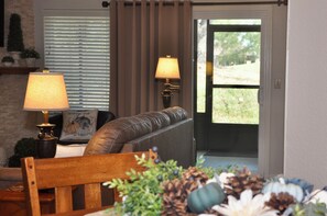 A living room with a brown leather sofa, two lamps, a wooden chair, and a door leading outside.