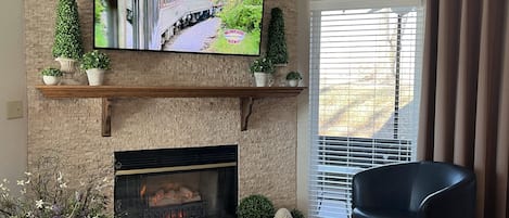 Sala de estar com lareira, televisão na parede e um espaço de estar confortável.