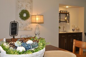 A dining area with a table set for two, a decorative centerpiece, a wall-mounted lamp, and a chalkboard sign.