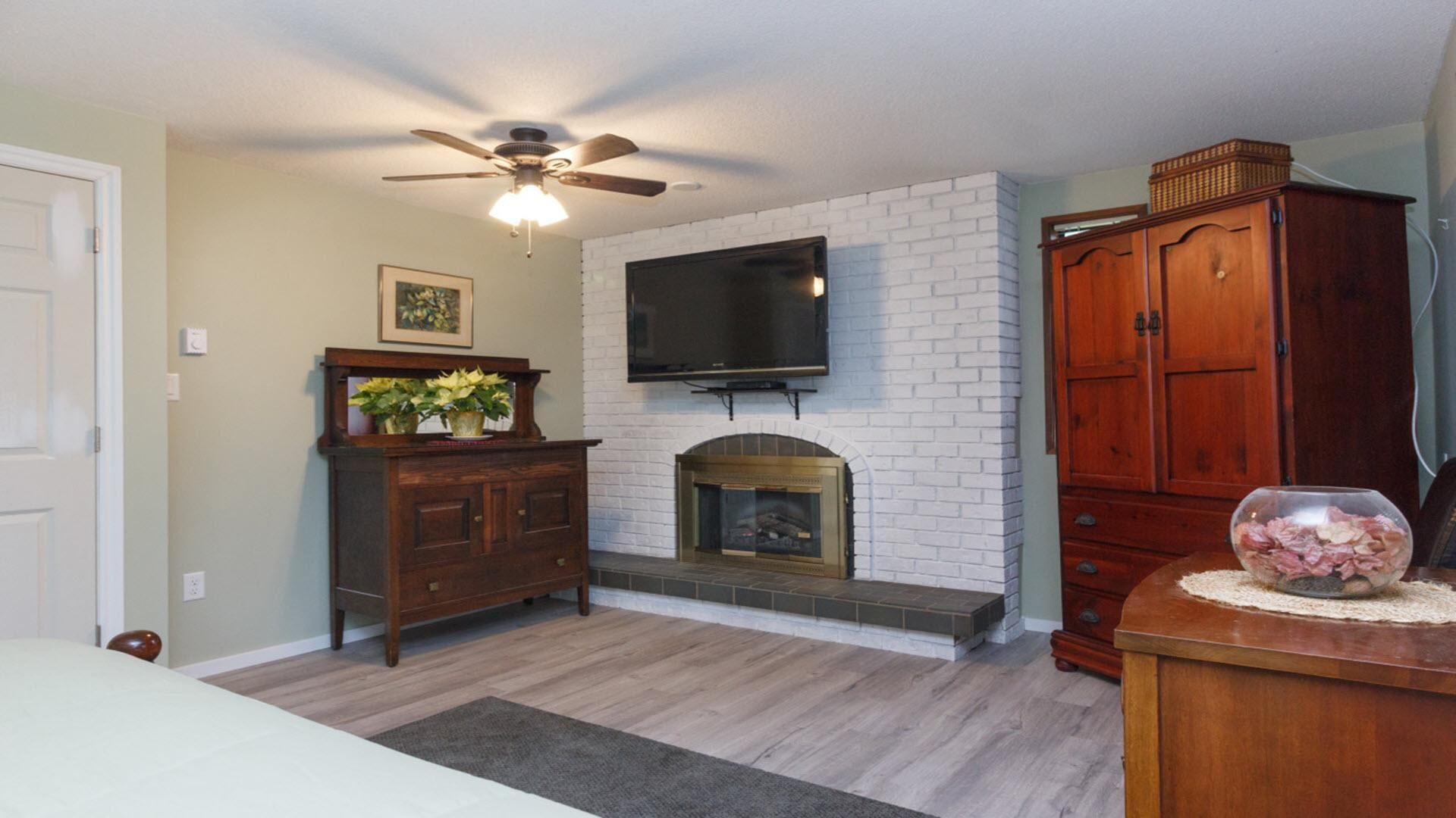 A living room with a fireplace, a television mounted on the wall, a ceiling fan, and wooden furniture.