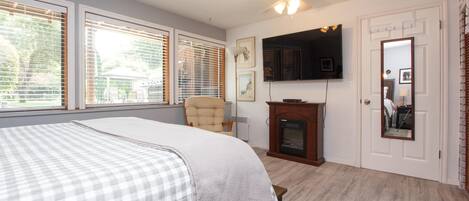 Ein Schlafzimmer mit Bett, Sessel, Kamin, Fernseher und einer Tür mit Spiegel.