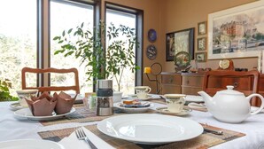 A dining table set with plates, cups, and a teapot, surrounded by chairs and a plant.
