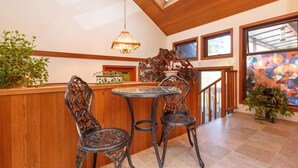 A dining area with a round table and two chairs, a hanging light fixture, and a view of the outside through large windows.