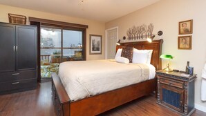A bedroom with a large bed, a wardrobe, a nightstand with a lamp, and a window with a view.