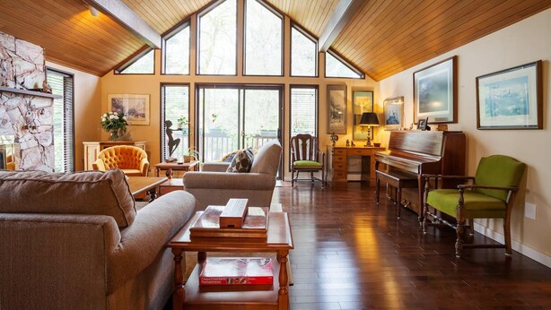 A spacious living room with a high ceiling, large windows, a piano, and a fireplace.