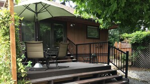 Una terraza de madera con mobiliario exterior, un espacio cubierto con mesa y sillas, y una escalera que lleva a un edificio.