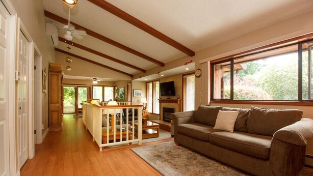Un salón amplio con suelo de madera, un ventanal grande, un sofá y una zona de comedor de madera.