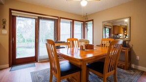 Un comedor con una mesa y sillas de madera, un ventilador de techo y vistas a través de puertas correderas de vidrio.