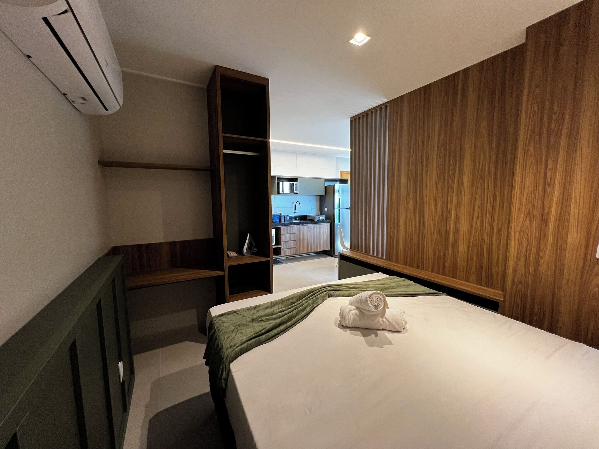 Ein Hotelzimmer mit Bett, einer grünen Decke, einem Handtuch, einem Holzschrank und Blick auf die Küche.