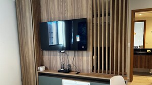 Ein modernes Wohnzimmer mit Flachbildfernseher an einer Holzwand, Geschirrspüler und einem weißen Sessel.