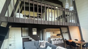 A spacious loft with a large gray sectional sofa, a dining area with a wooden table and chairs, and a kitchen in the background. - Cozy 3-Level cabin in Groveland with WiFi, stunning views, deck and hot tub (Groveland)