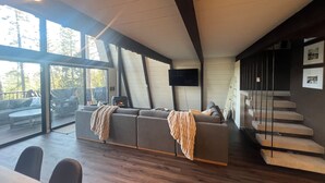 A modern living room with a large grey sofa, a flat-screen TV, and a fireplace. - Cozy 3-Level cabin in Groveland with WiFi, stunning views, deck and hot tub (Groveland)