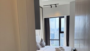 Habitación de hotel moderna con una cama grande, un escritorio y vistas de la ciudad a través de amplios ventanales.