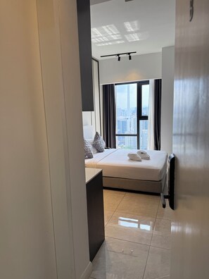 A modern hotel room with a large bed, a desk, and a view of the cityscape through large windows. - Residence Axon Bukit Bintang by TaheeenS (Kuala Lumpur)