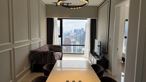 Una sala de estar moderna con un sofá, una mesa de comedor y un televisor. Hay un ventanal con vistas a la ciudad.