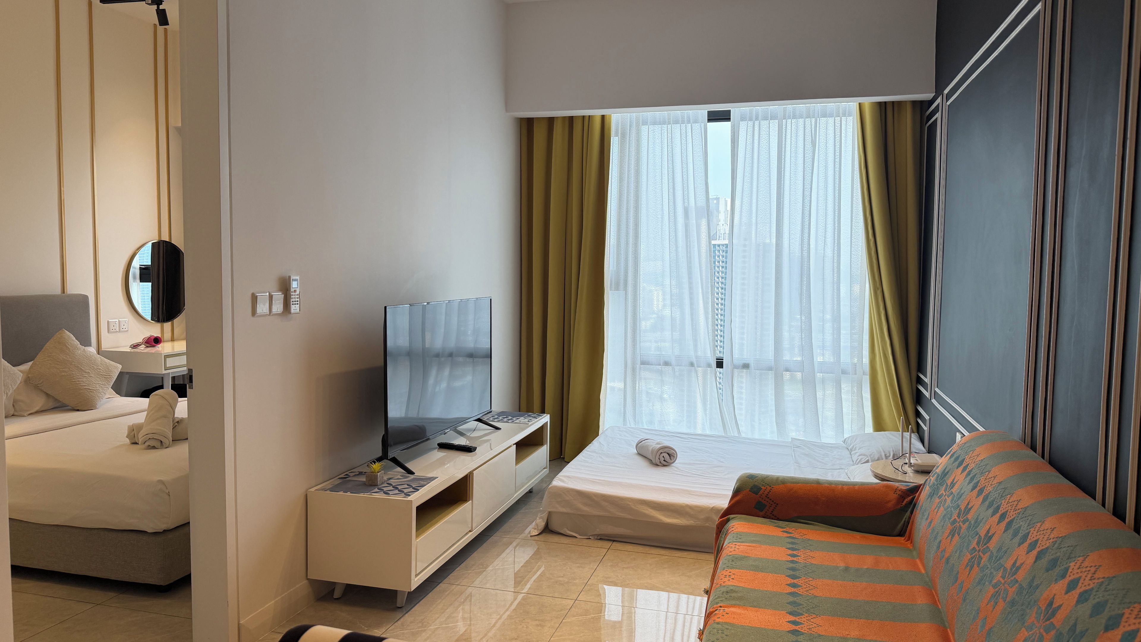 Habitación de hotel con cama, sofá, televisión, escritorio y ventana con cortinas.