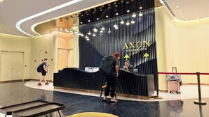 Zona de recepción de hotel con diseño moderno, que presenta un mostrador negro, una pantalla digital y un letrero que dice "AXON RESIDENCE".