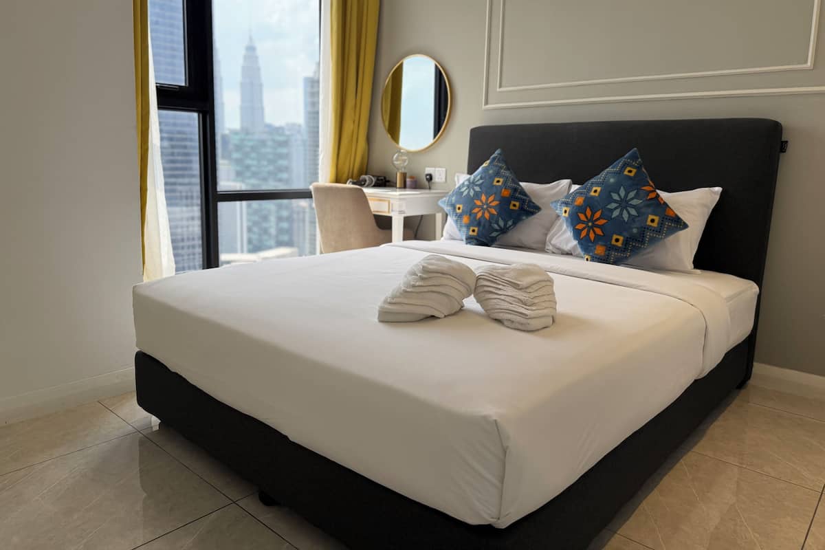 Ein Hotelzimmer mit einem großen Bett, einem Schreibtisch, einem Sessel und Blick auf eine Skyline durch ein großes Fenster.