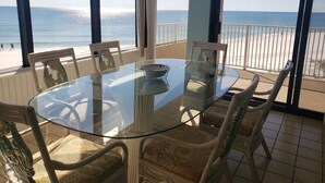 A glass-top table with chairs in a room with a view of the beach.