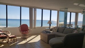 A living room with a large window overlooking the sea, a sofa, a chair, and a small table.