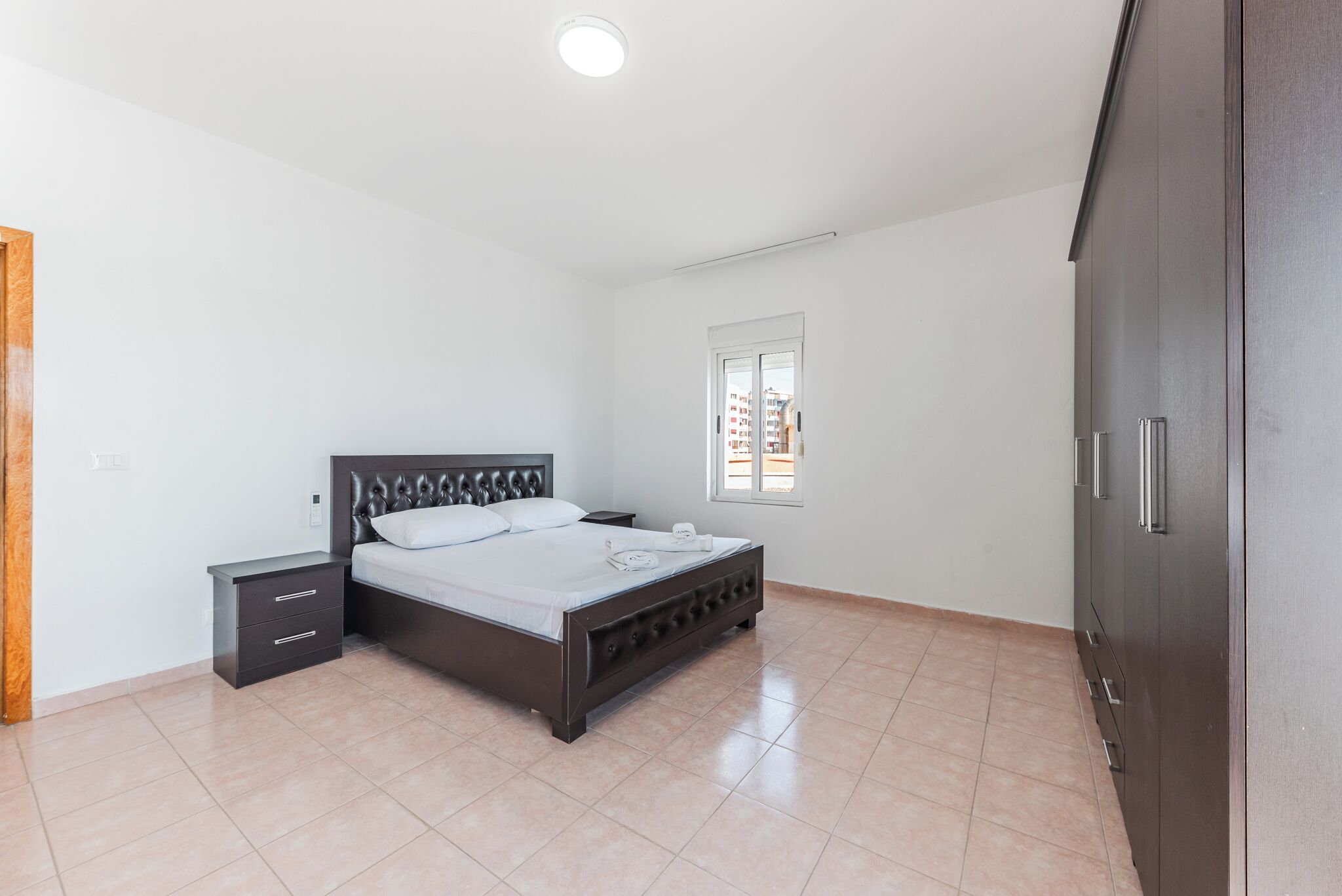 A bedroom with a bed, a nightstand, a wardrobe, and a window.